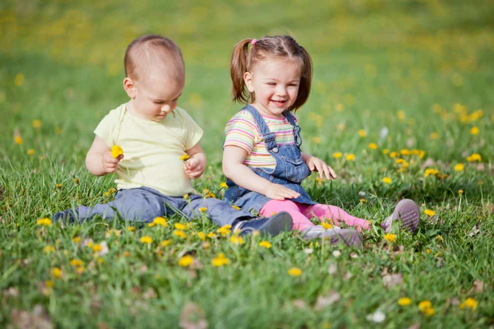 2 kids sitting in the grass and playing with the flowers